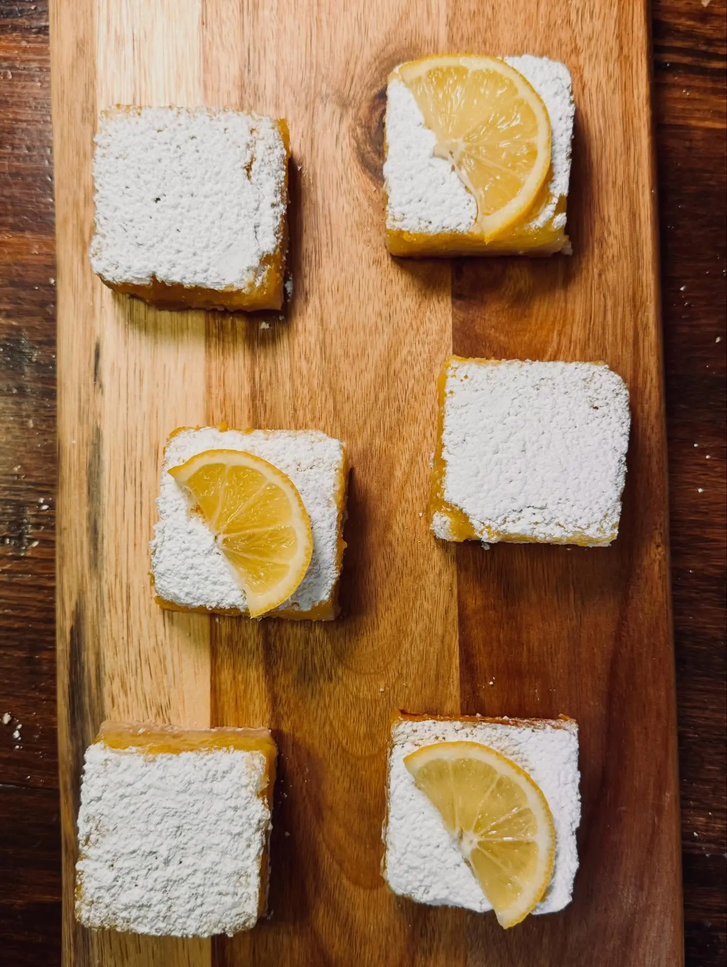 Powdered lemon bars arranged on a wooden serving board